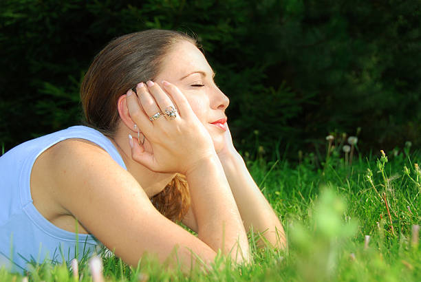 Young beautiful woman of 20s lying in the grass, looking at camera and smiling. Portrait only. 