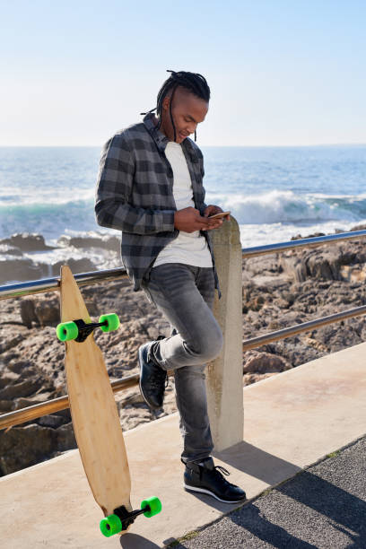 istock Young mixed race skateboarder looking at his smartphone by the ocean 932794030