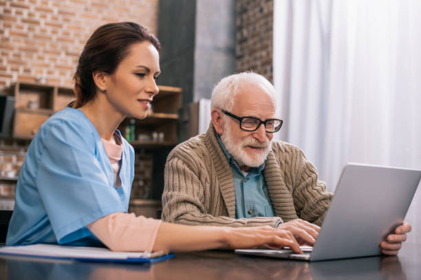 Nurse sitting by senior man using laptop