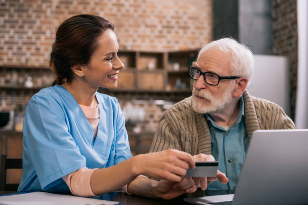 Nurse helping senior patient using laptop and credit card Nurse helping senior patient using laptop and credit card hospice photos stock pictures, royalty-free photos & images