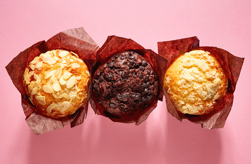 Assorted muffins in brown paper on pink background, top view