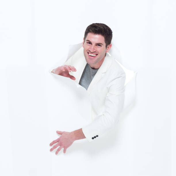 istock Handsome man in white suit breaking through paper 933108482