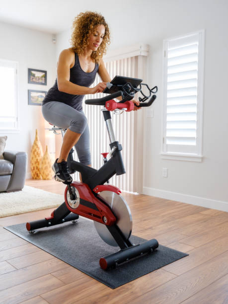 Woman Exercising on Spin Bike in Home A woman exercising on a spin bike using an online instructor inside a home. spin bike stock pictures, royalty-free photos & images