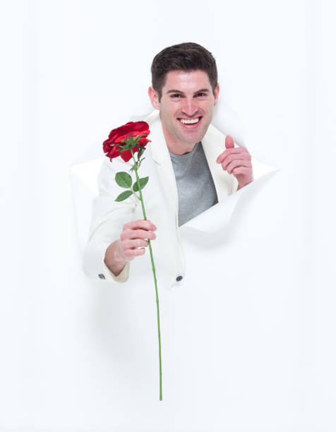 istock Handsome man in white suit breaking through paper holding one rose 933109252