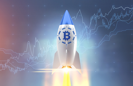 White and blue rocket with a bitcoin symbol starting up. A blurred blue background with graphs. Toned image double exposure