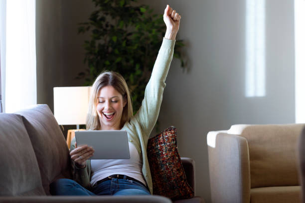 istock Beautiful young woman celebrating a success while using her digital tablet at home. 933123032