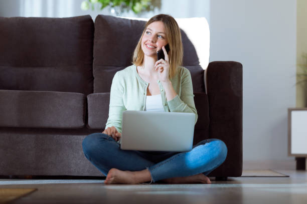 istock Beautiful young woman using her smartphone while working with laptop at home. 933123214