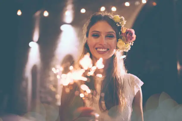 Happy smiling boho bride having fun celebrating with sparklers at night rustic wedding reception