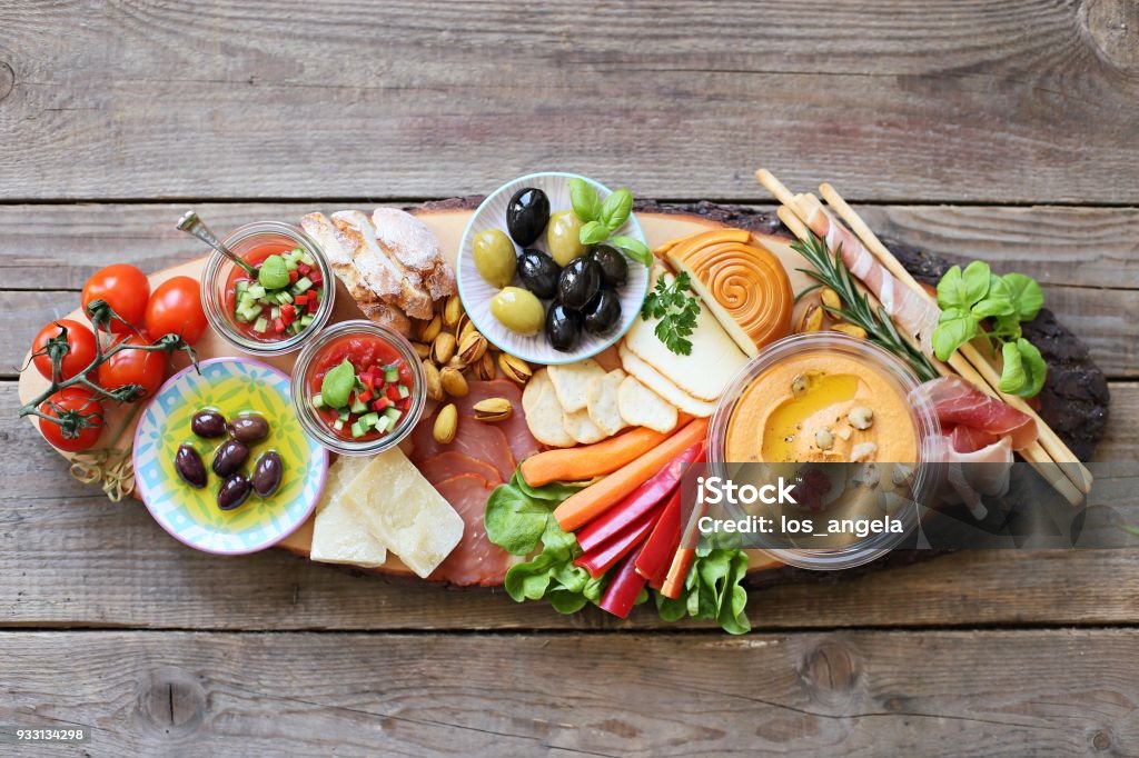 Appetizers table with cured meat, gazpacho soup, jamon, olives, cheese, hummus and vegetables. Mediterranean diner table with tapas selection. Appetizers table with cured meat, gazpacho soup, jamon, olives, cheese, hummus and vegetables. Mediterranean diner table with antipasto selection. Overhead view. Appetizer Stock Photo