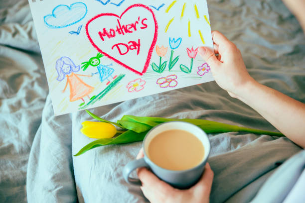 młoda matka dostać niespodzianka prezent na dzień matki w łóżku. kobieta trzyma zdjęcie swojego dziecka na dzień matki - mothers day tulip yellow greeting card zdjęcia i obrazy z banku zdjęć