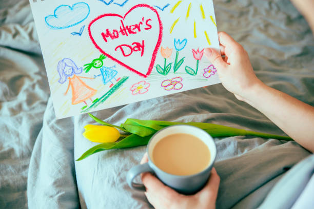 молодая мать получить сюрприз подарок для матери день в постели. женщина держать картину своего ребенка на день матери - mothers day tulip yellow greeting card стоковые фото и изображения