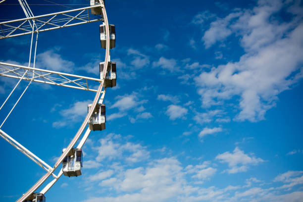 istock Horizontal View of a White Ferris Wheel on Partially Cloudy Sky Background 933140640