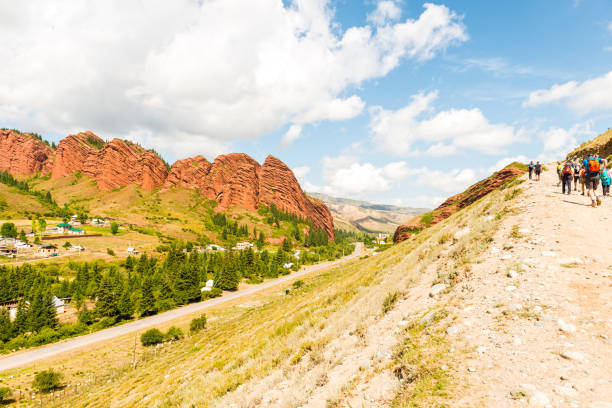Line of small group of people hiking on the edge of dirt slope against blue sky at picturesque Jeti-Oguz gorge located 28 kilometers to the south-west of the town of Karakol. Its name is translated from Kyrgyz language means “Seven bulls”. Low angle view on sunny day.