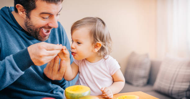 istock Father feeding toddler with spoon on table 933167100