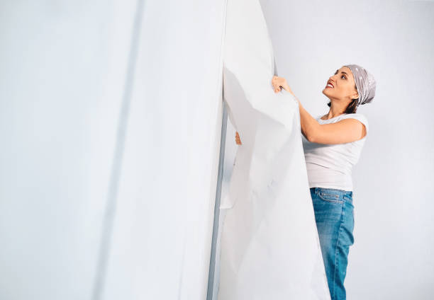 Woman prepare room for renovation, take off wallpapers from wall