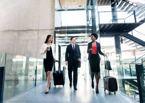 Latin executives walking with suitcases and hand luggage Cheerful multi-ethnic young business people walking side by side with suitcases, looking at each other and smiling. business travel stock pictures, royalty-free photos & images