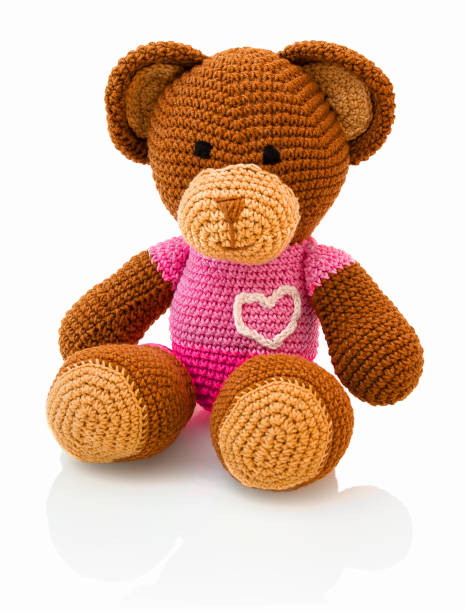 Cute handmade crochet bear doll isolated on white background with shadow reflection. Playful crochet brown pinky bear sitting on white underlay. Knitted bear.