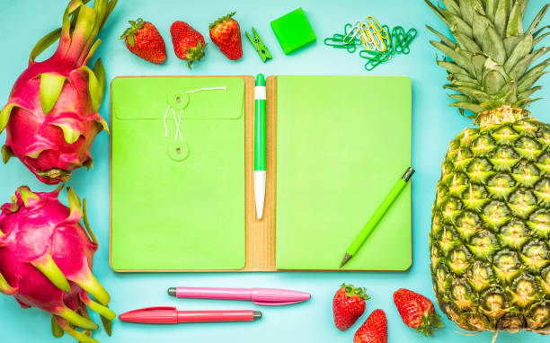 Blank green notebook with tropical fruit and accessories laying on blue table.Home office,workspace design backgrounds,flat lay,top view