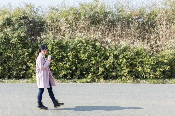 istock side view of young female holding disposable cup walking against trees 933294626