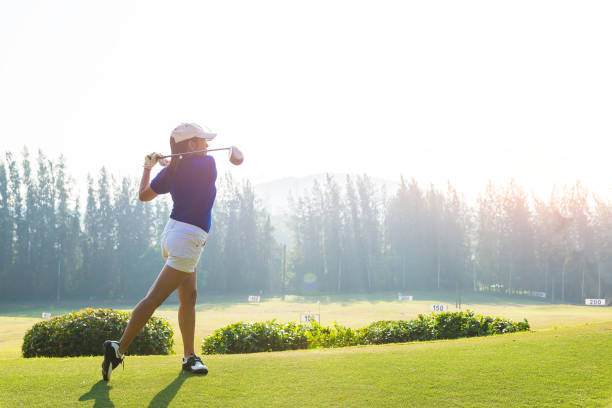 kobieta golfista w akcji końca downswing kierowcy drewna, po uderzeniu piłkę golfową z dala od tee off do toru wodnego przed, zachód słońca scenerii w tle - rules of golf zdjęcia i obrazy z banku zdjęć