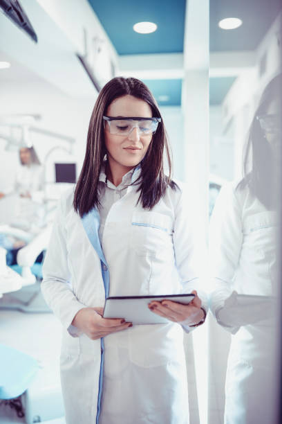 istock Cute Smiling Dentist With Tablet and Protective Eyewear Working in Dental Office 933314232