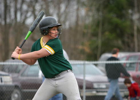One Sportive Caucasian Female Baseball Player Athlete Tossing Up Ball with Bat wearing Sport Outfit Against Pure White background. Vertical Image