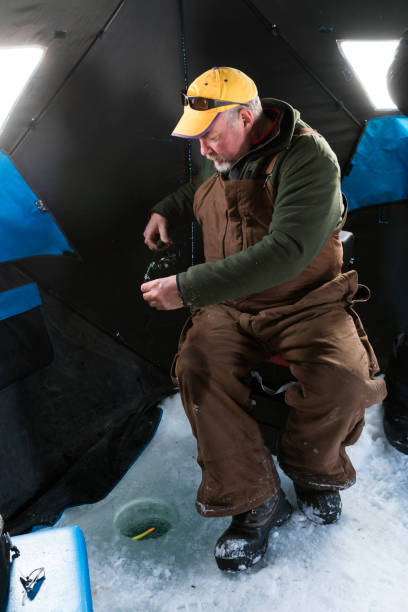 Ice fishing in northern Minnesota Man in his 50s sets his fishing line inside a small hole drilled into the ice of the frozen lake while ice fishing from his hut on a cold subzero winter day, Hackensac, Minnesota, USA man ice fishing stock pictures, royalty-free photos & images