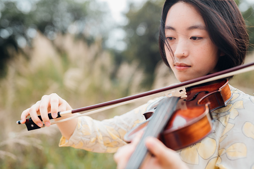 Asian teenage girl playing a violin in nature background.
