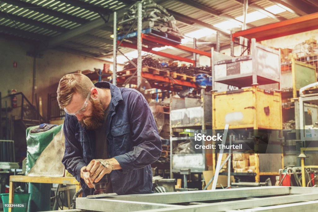 Young Metal Worker Using Power Tool In Factory With Protective Equipment Young Australian Apprentice Metal Worker In Factory Australia Stock Photo