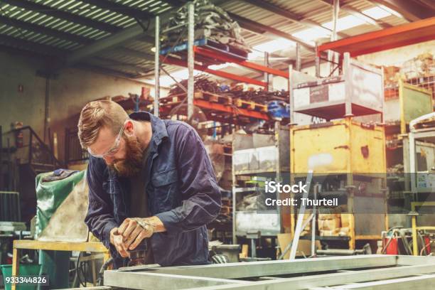 Young Metal Worker Using Power Tool In Factory With Protective Equipment Stock Photo - Download Image Now