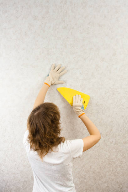 istock woman smoothing wallpaper with spatula 933365410