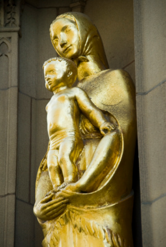 Looking out onto a busy street,an unusual statue of the Blessed Virgin and Child,on an outer wall of the Cathedral in Manchester,north of England.She is dressed as a Lancashire  mill worker of the nineteenth century,with shawl around her shoulders,and headscarf tied in a knot under  her chin.The statue is gilded, and stands in a niche on the ancient building.