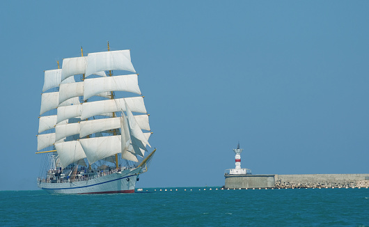 Bark with white sails in the Black Sea enters the Crimea harbor in summer