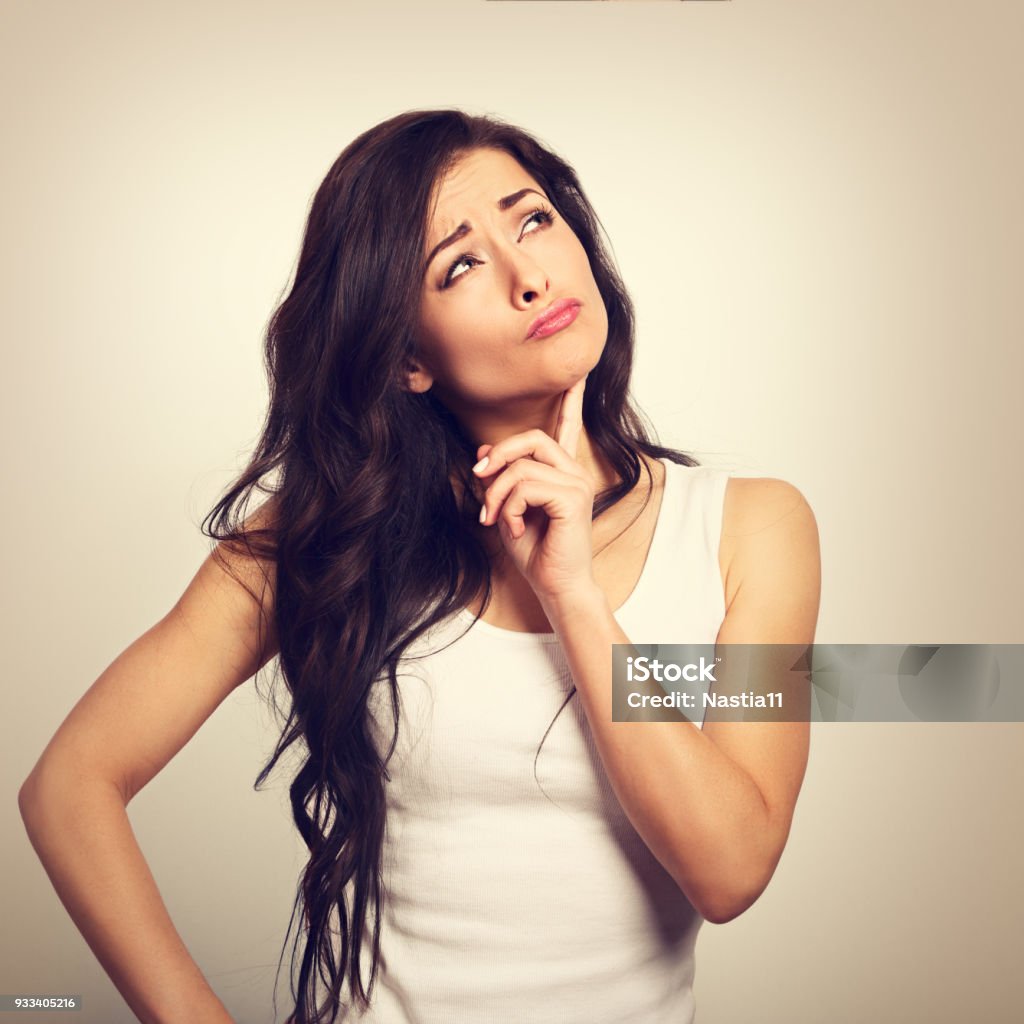 Confusion grimacing brunette woman thinking and looking up in white t-shirt. Toned closeup portrait Adult Stock Photo