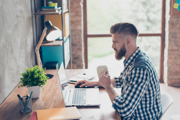 istock Handsome focused concentrated thinking pondering pensive browsing reading chatting online email playing accountant drinking tea using netbook for checking post networking at workplace 933405296