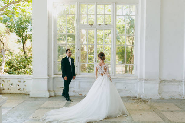 beau mariage photosession. marié en costume noir et jeune mariée en robe de dentelle blanche avec panache long avec une coiffure exquis en intérieur vintage sur la véranda d’une vieille maison avec des colonnes - veil bride lace married photos et images de collection