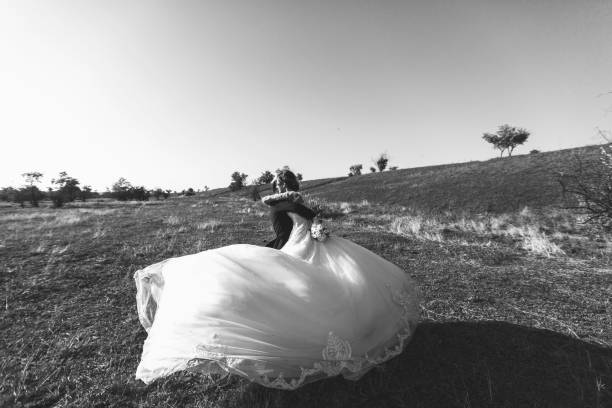 beau mariage photosession. beau marié en costume et lunettes encerclant pour sa jeune épouse de bras en robe de dentelle avec coiffure exquis pour une promenade autour de grand champ contre le ciel. noir et blanc - veil bride lace married photos et images de collection