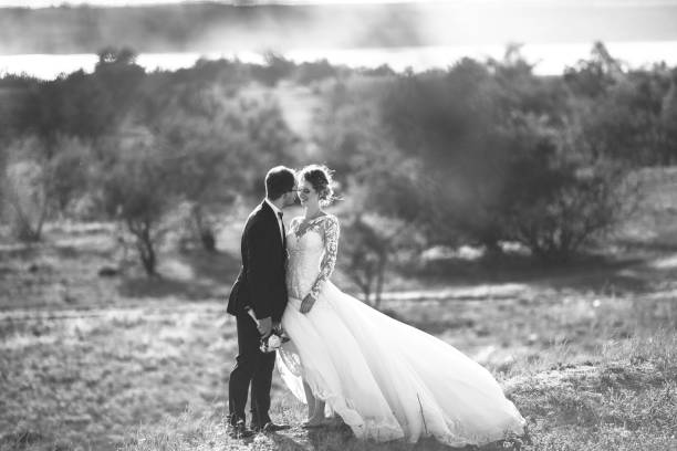 beau mariage photosession. beau marié dans un costume noir et une jeune mariée en robe de dentelle avec coiffure exquise promenade autour du terrain de grand fond d’arbres et arbustes. noir et blanc - veil bride lace married photos et images de collection