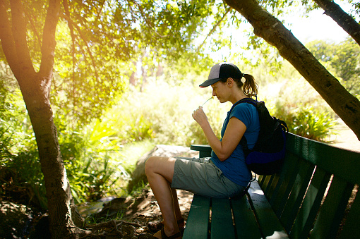 A female hiker with a backpack and cap sitting in the shade on a bench smelling a flower on Paarl Rock Paarl Cape Winelands Cape Town South Africa