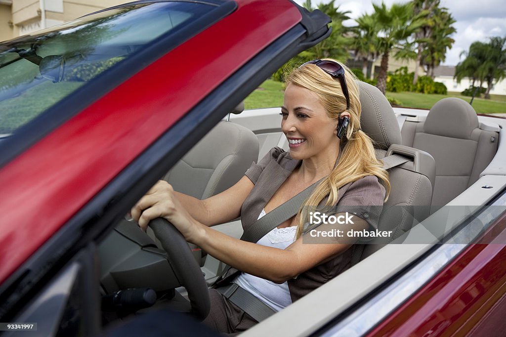 Beautiful Young Woman Driving Convertible Car Talking on Bluetooth Headset A beautiful young blond woman driving her convertible car and talking on her cell phone with a bluetooth headset Businesswoman Stock Photo