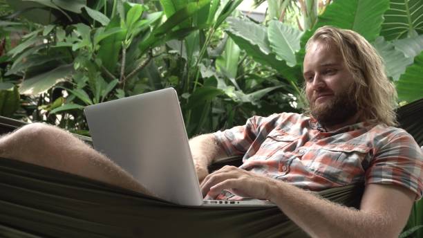 istock Man laying in hammock using laptop and smiling 933425508