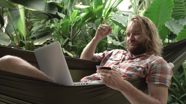 istock Man made successful payment with credit card and laptop while sitting on hammock 933425564