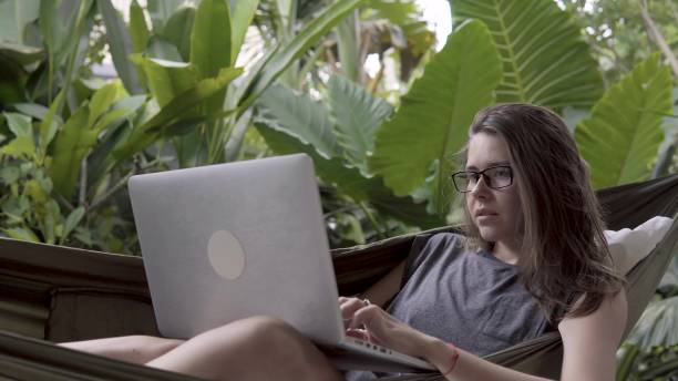 istock Woman working on laptop while sitting on hammock, exotic background 933427788