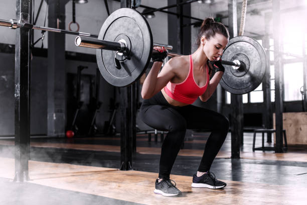 menina com um sino-bar em um ginásio de levantamento de peso - crouching exercising women barbell - fotografias e filmes do acervo