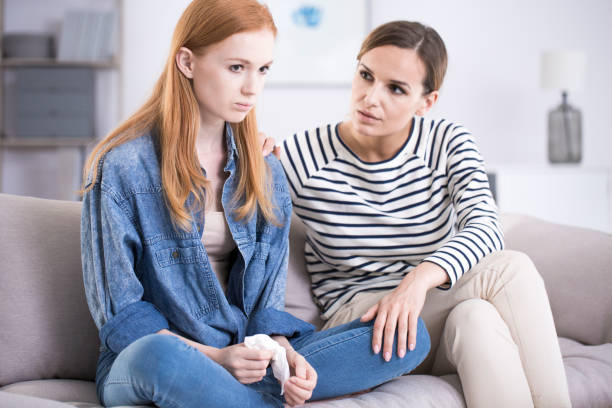 Woman comforting emotional teenage girl Woman comforting an emotional young teenage girl sitting with her legs crossed on a sofa and crying anorexia nervosa stock pictures, royalty-free photos & images