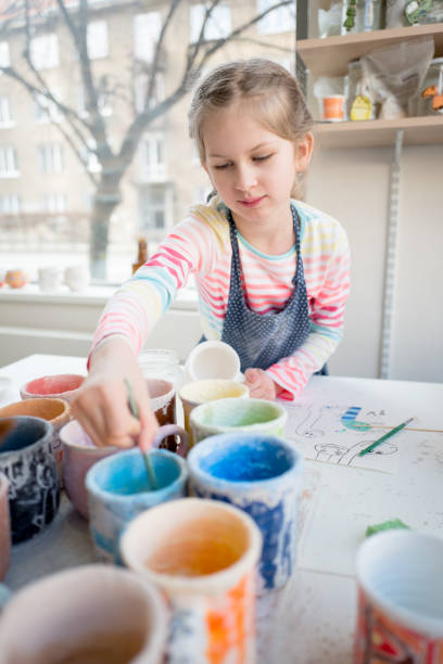 istock Young girl painting in pottery workshop using colourful paints and brush 933438262