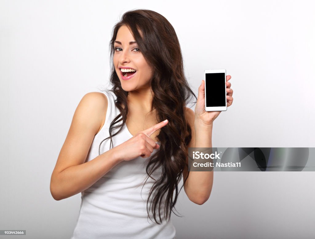 Happy smiling beautiful makeup woman holding and advertising mobile phone on white background with empty copy space. Closeup portrait Mobile Phone Stock Photo