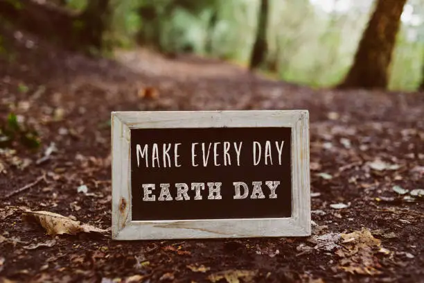closeup of a wooden-framed chalkboard with the text make every day earth day written in it, on the ground in the woods