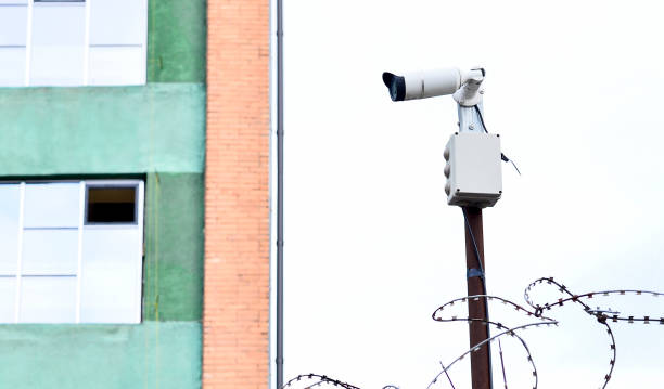 istock Camera video surveillance on the building background mounted on a brick wall, fenced with barbed wire. 933445900