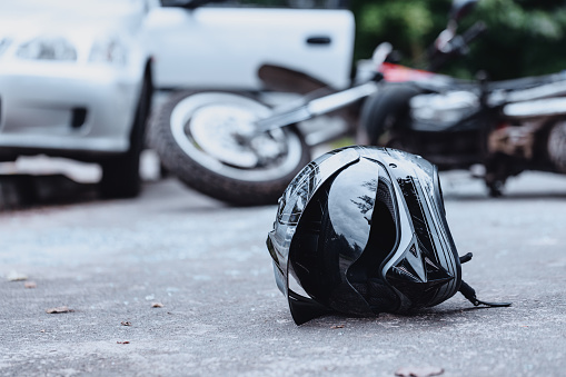 Close-up of a black biker helmet on the street with overturned motorbike in the background. Road collision concept